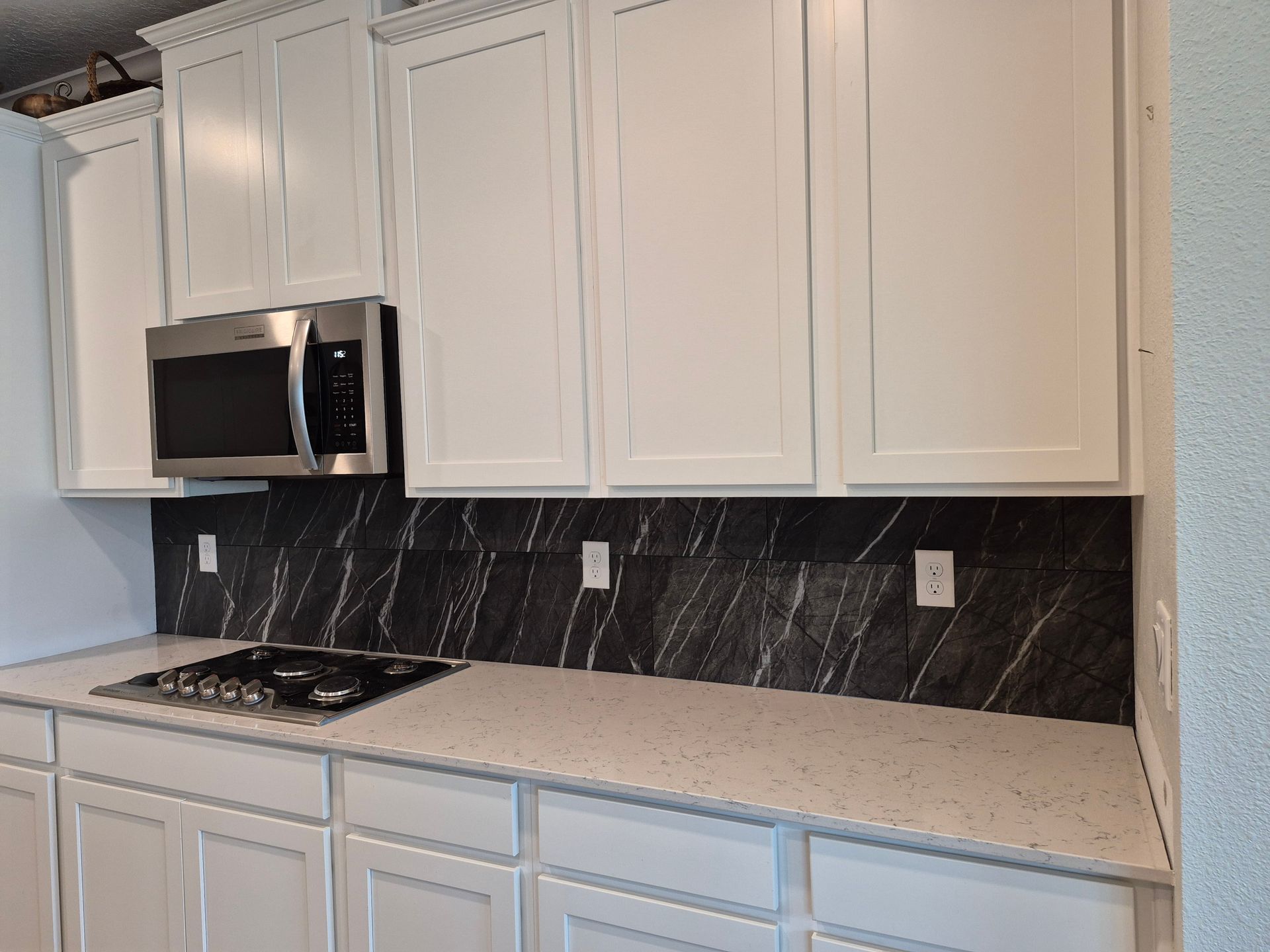 White kitchen cabinets, black marble backsplash, and stainless stove with microwave above.