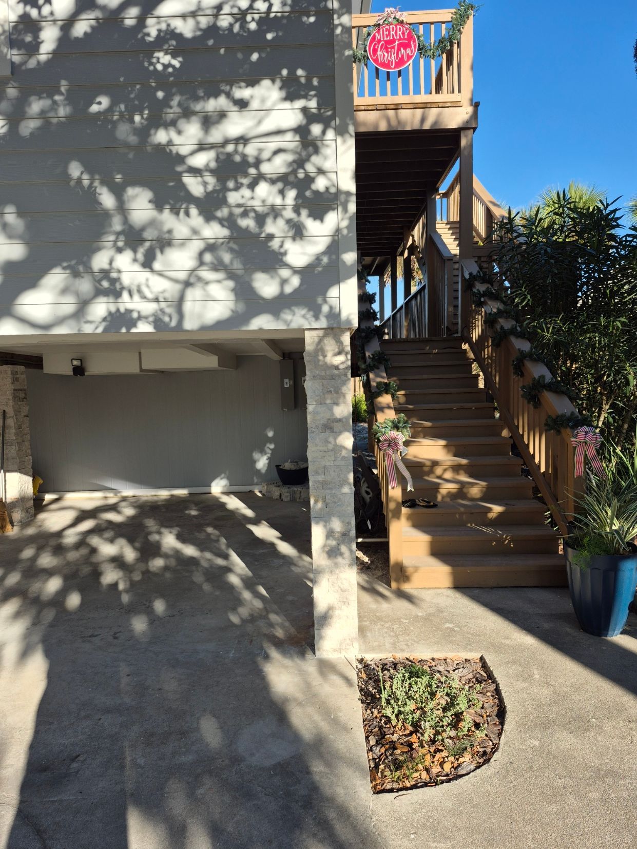 Exterior stairway beside a building, with potted plants and dappled sunlight on the wall and ground