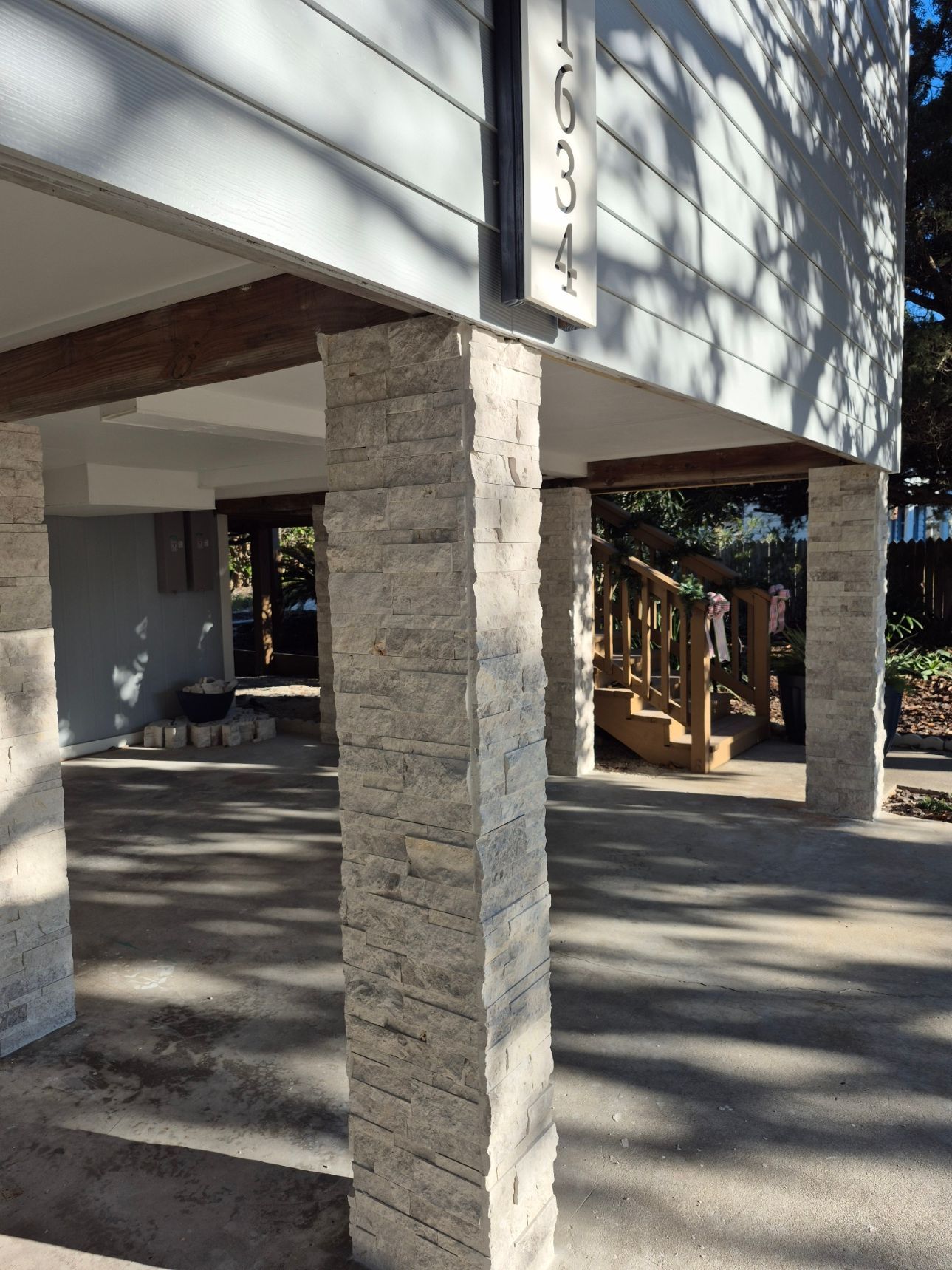 Stone columns supporting a shaded building entrance with dappled sunlight on the pavement