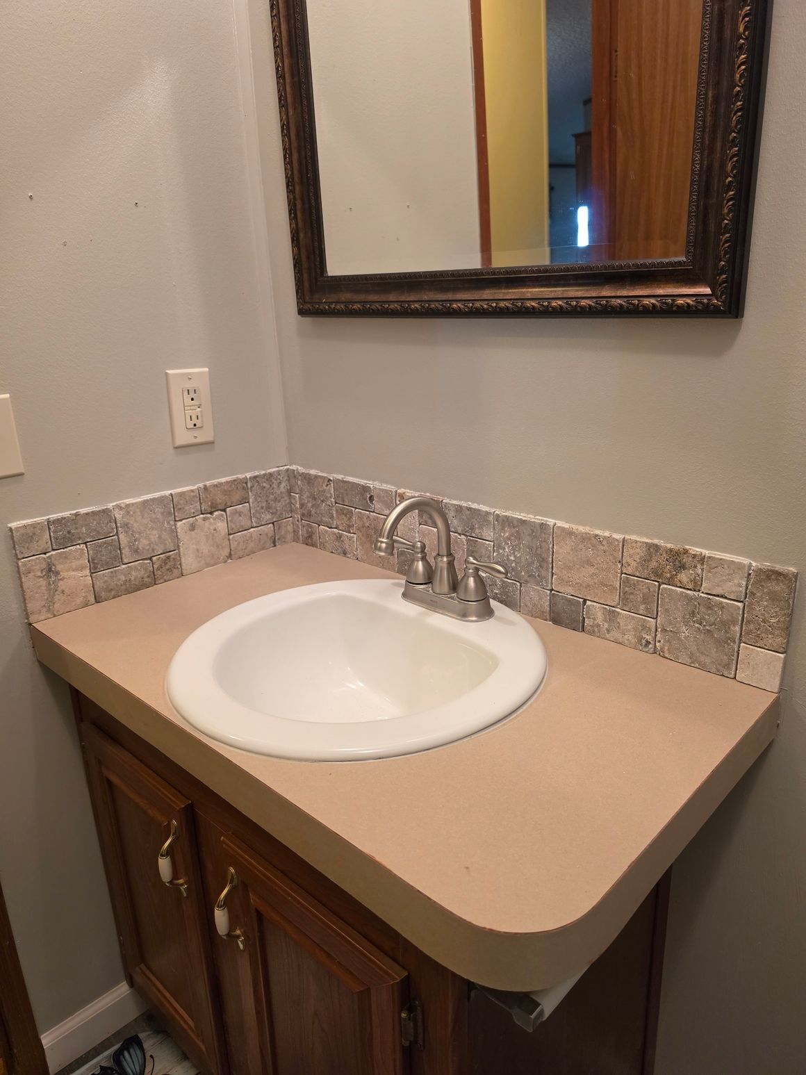 Bathroom vanity with a white sink, tan countertop, wood cabinet, and wall mirror