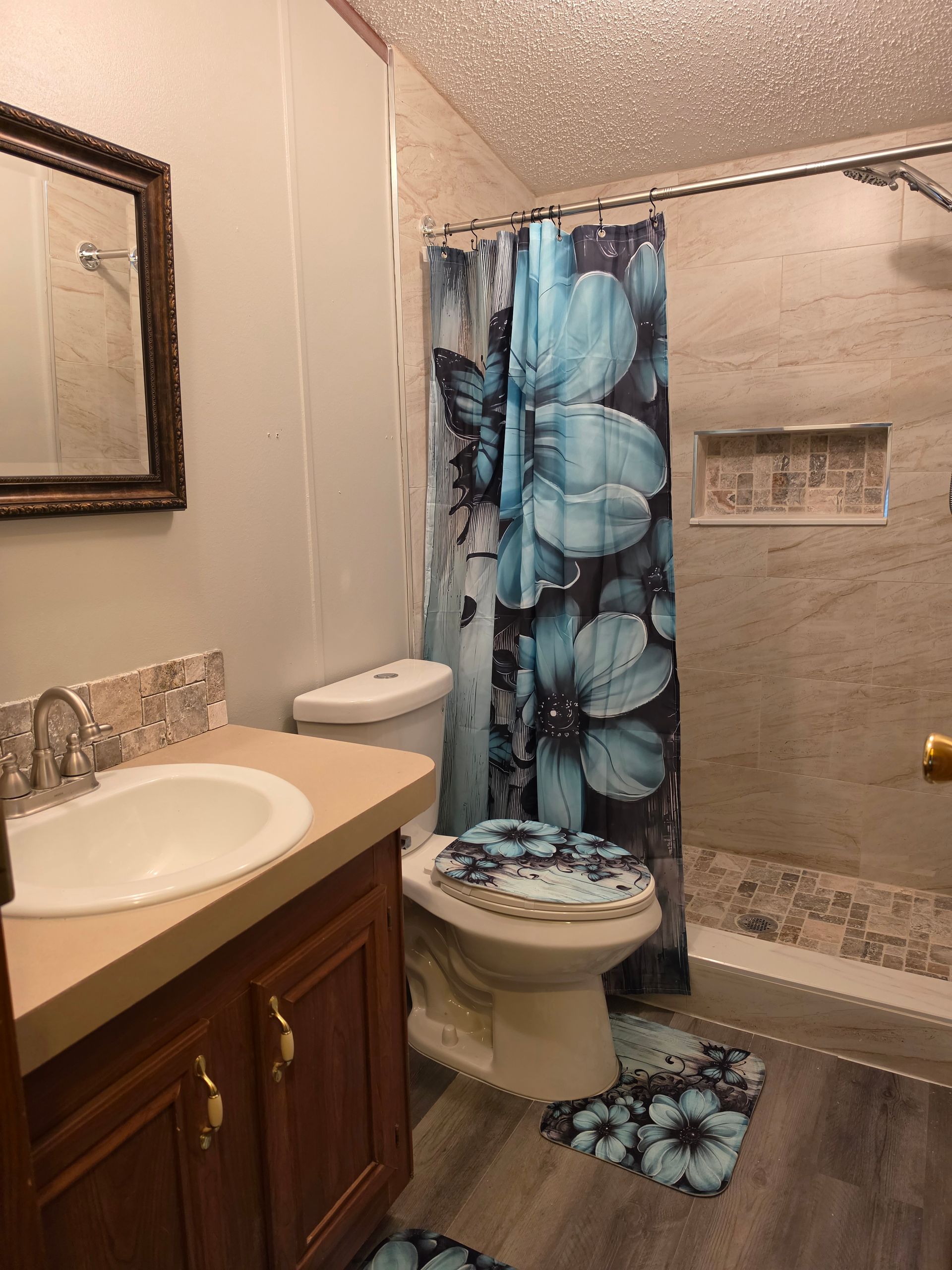 Bathroom with sink, toilet, shower, and blue floral shower curtain and rug.