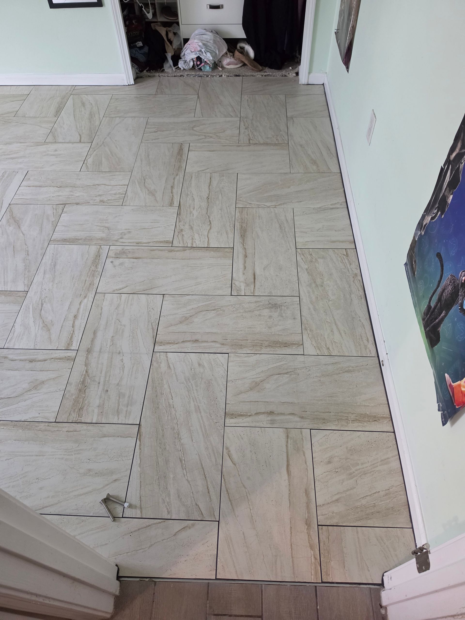 Hallway with light herringbone tile floor, white walls, and a small dog near the doorway.
