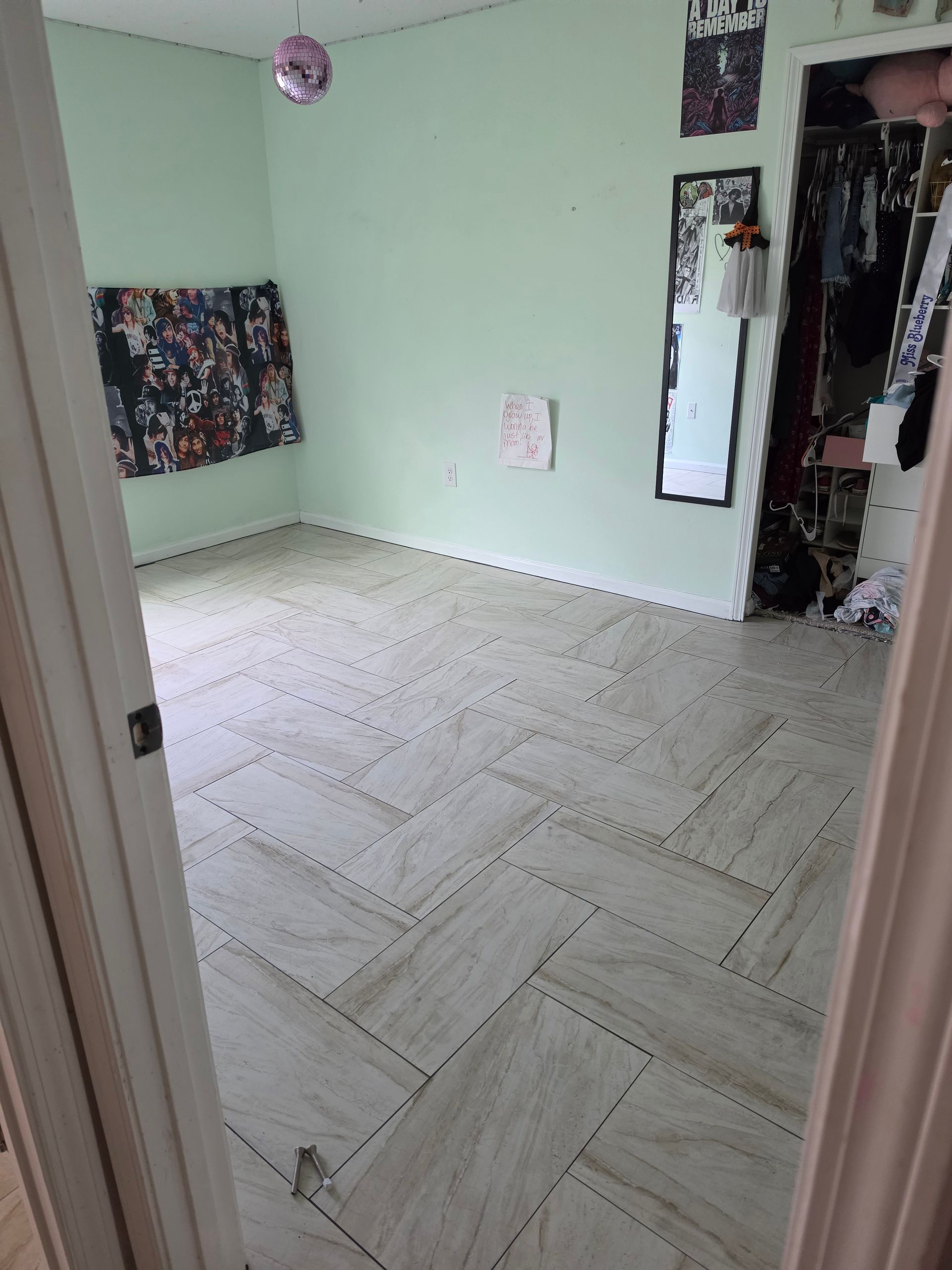 Empty bedroom with pale green walls, light wood floor, and a mirror near the doorway.
