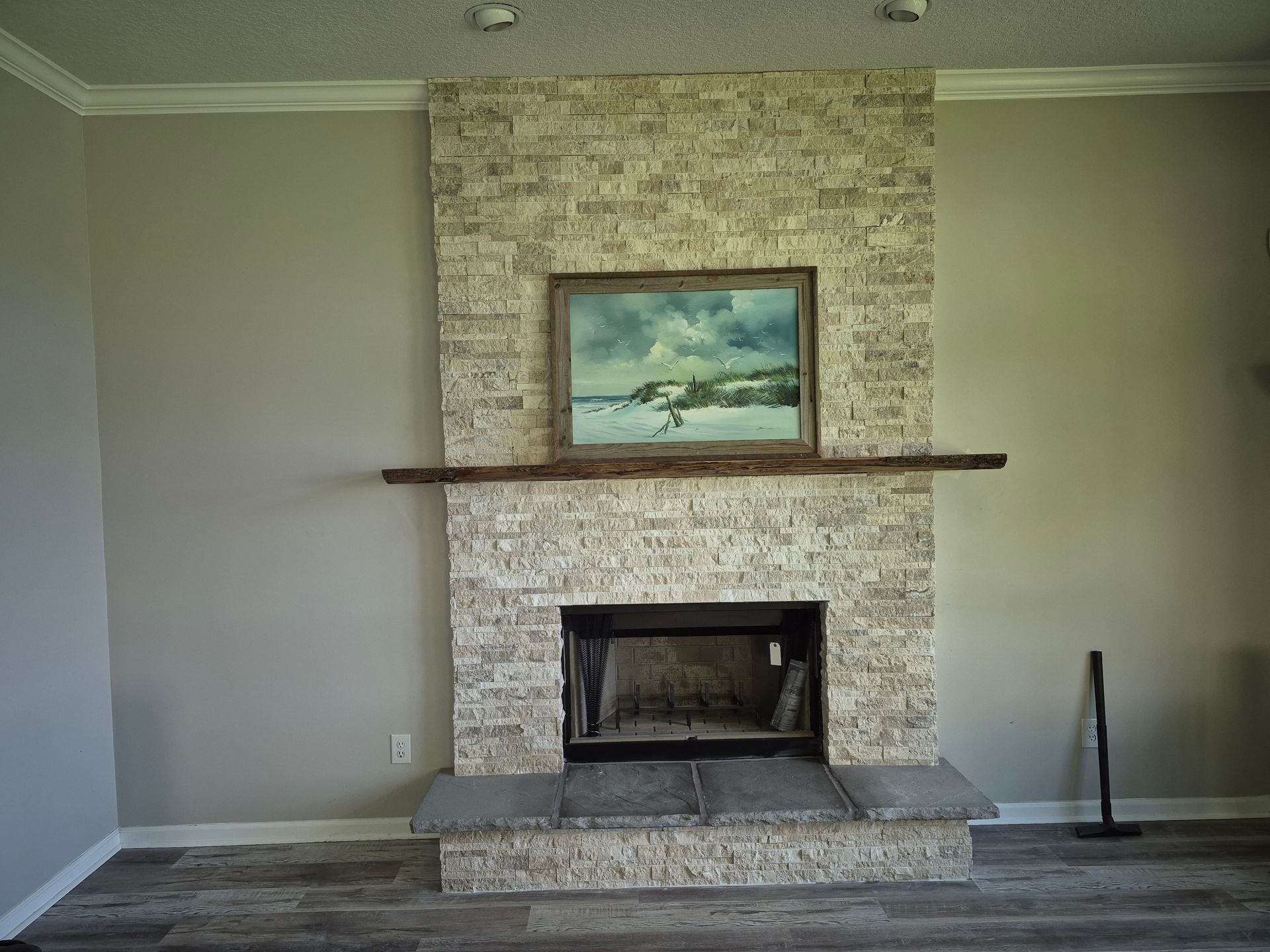 Living room with a stone fireplace, wooden mantel, and seascape painting centered on the wall