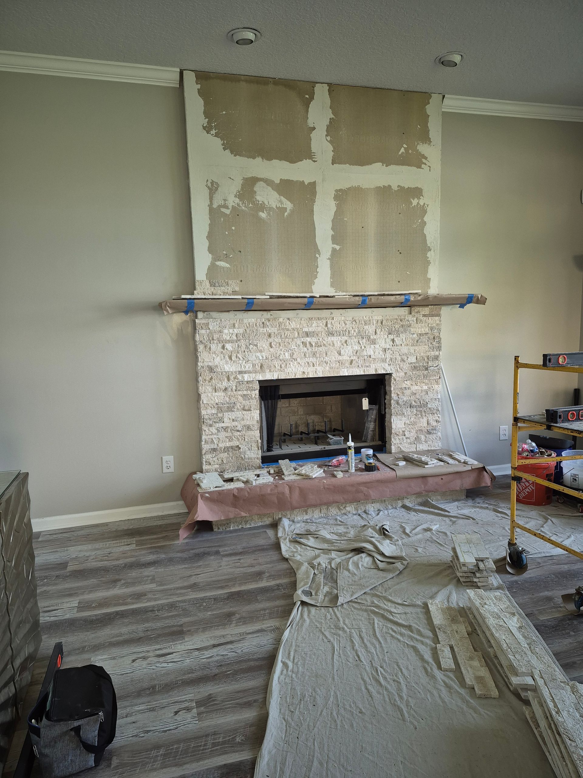 Living room under renovation with a fireplace, patched wall above, and drop cloths on the floor
