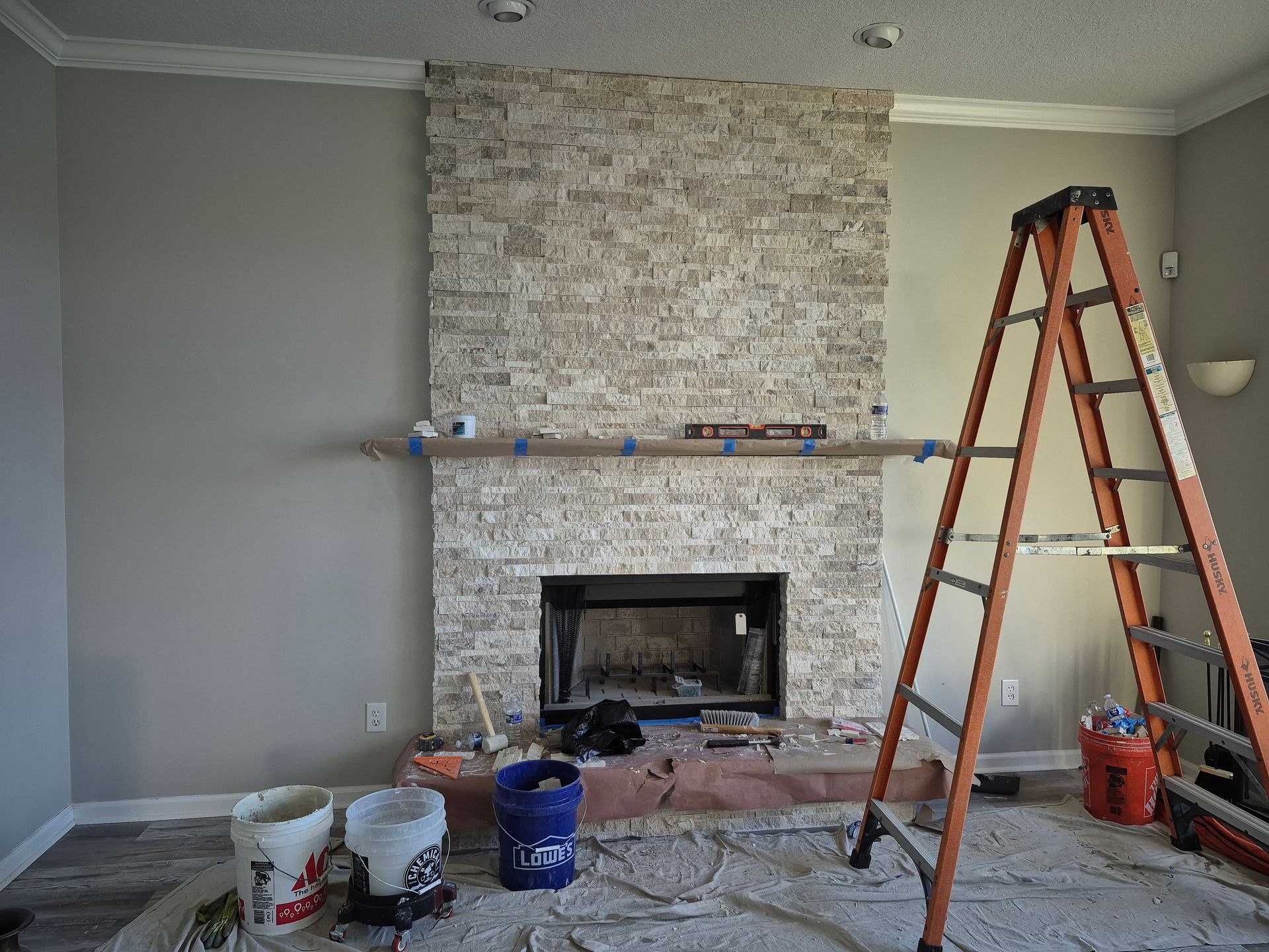 Living room fireplace under renovation with ladder, tools, and exposed stone wall.