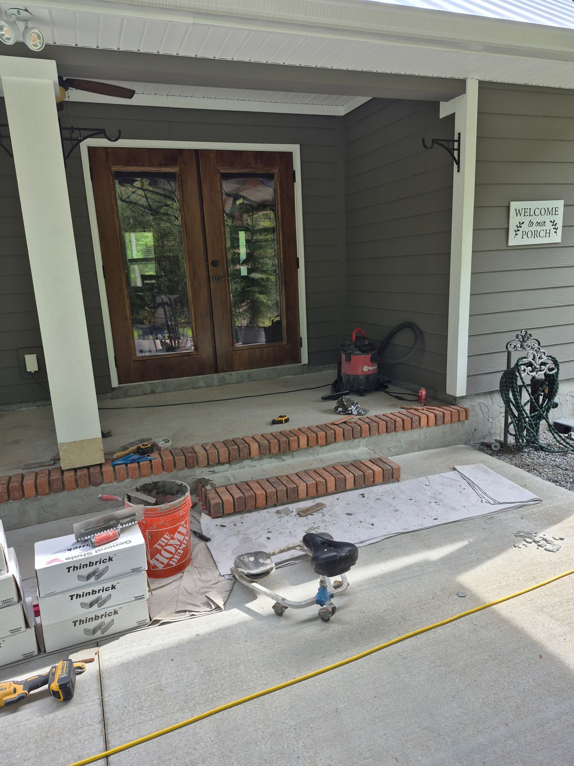 Front porch with tools, bricks, and materials arranged for a renovation project.