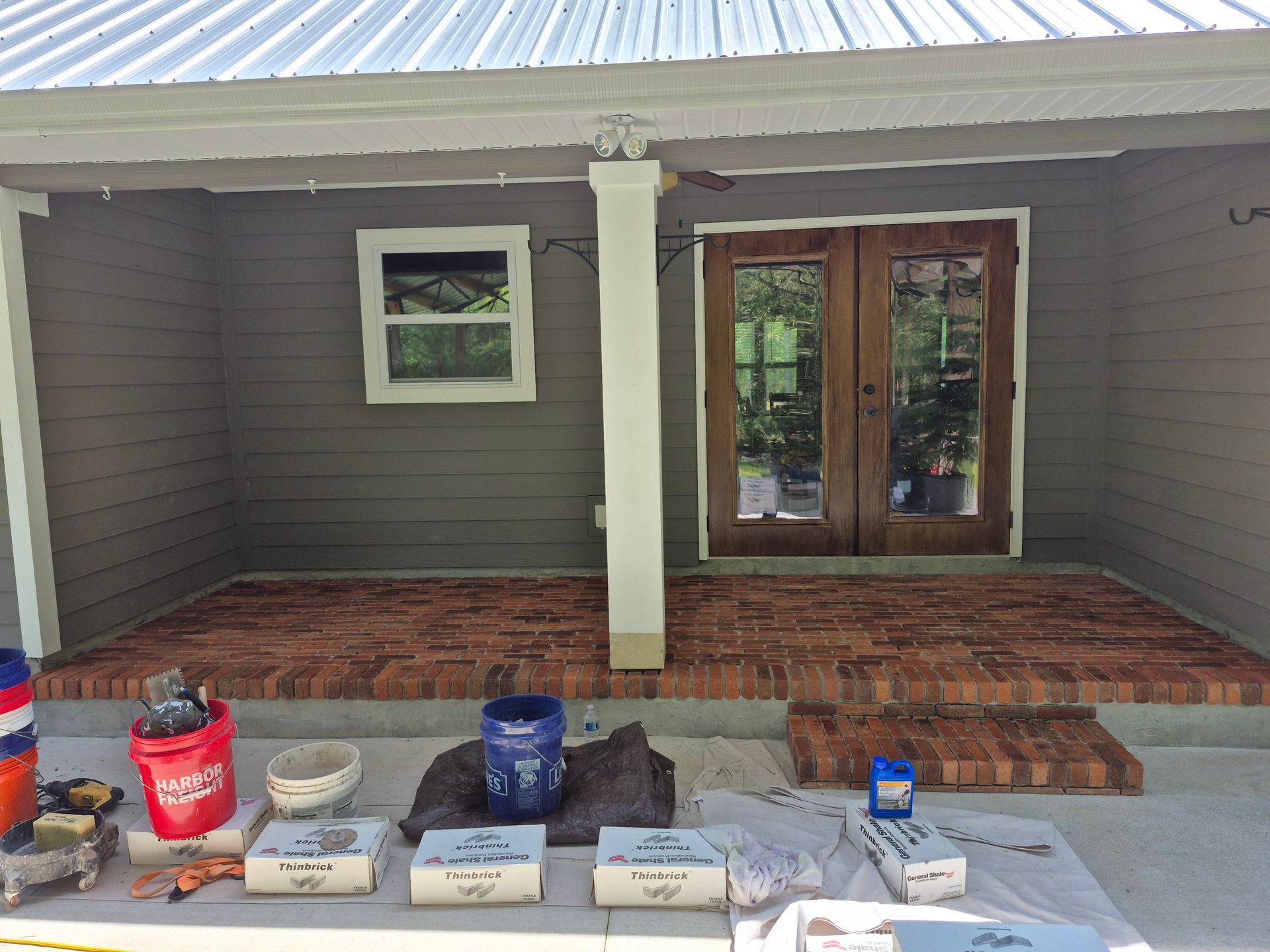 Front porch with paint supplies arranged on the steps and floor in front of double wooden doors.