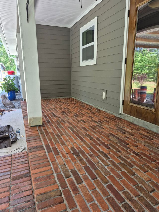 Brick porch with gray siding, white columns, and a glass door beside a single window.
