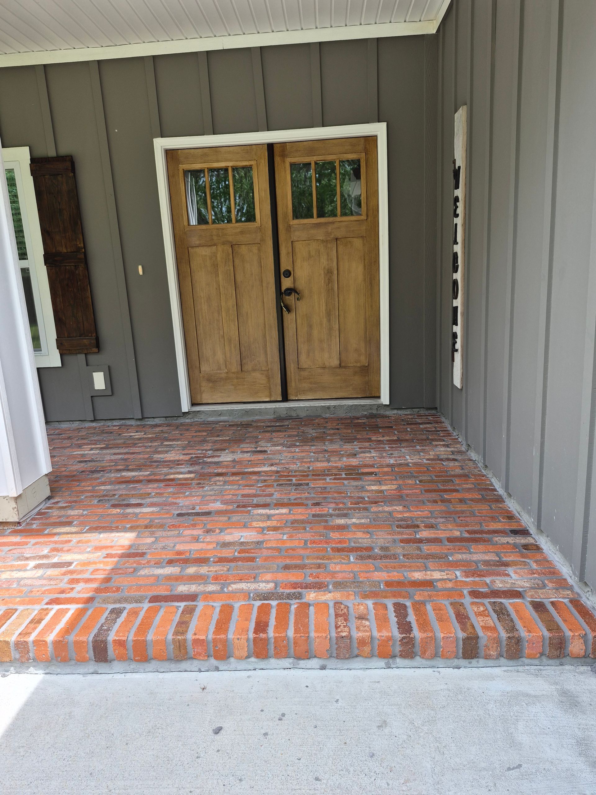 Brick front porch with wooden double doors and gray siding, viewed from the entryway