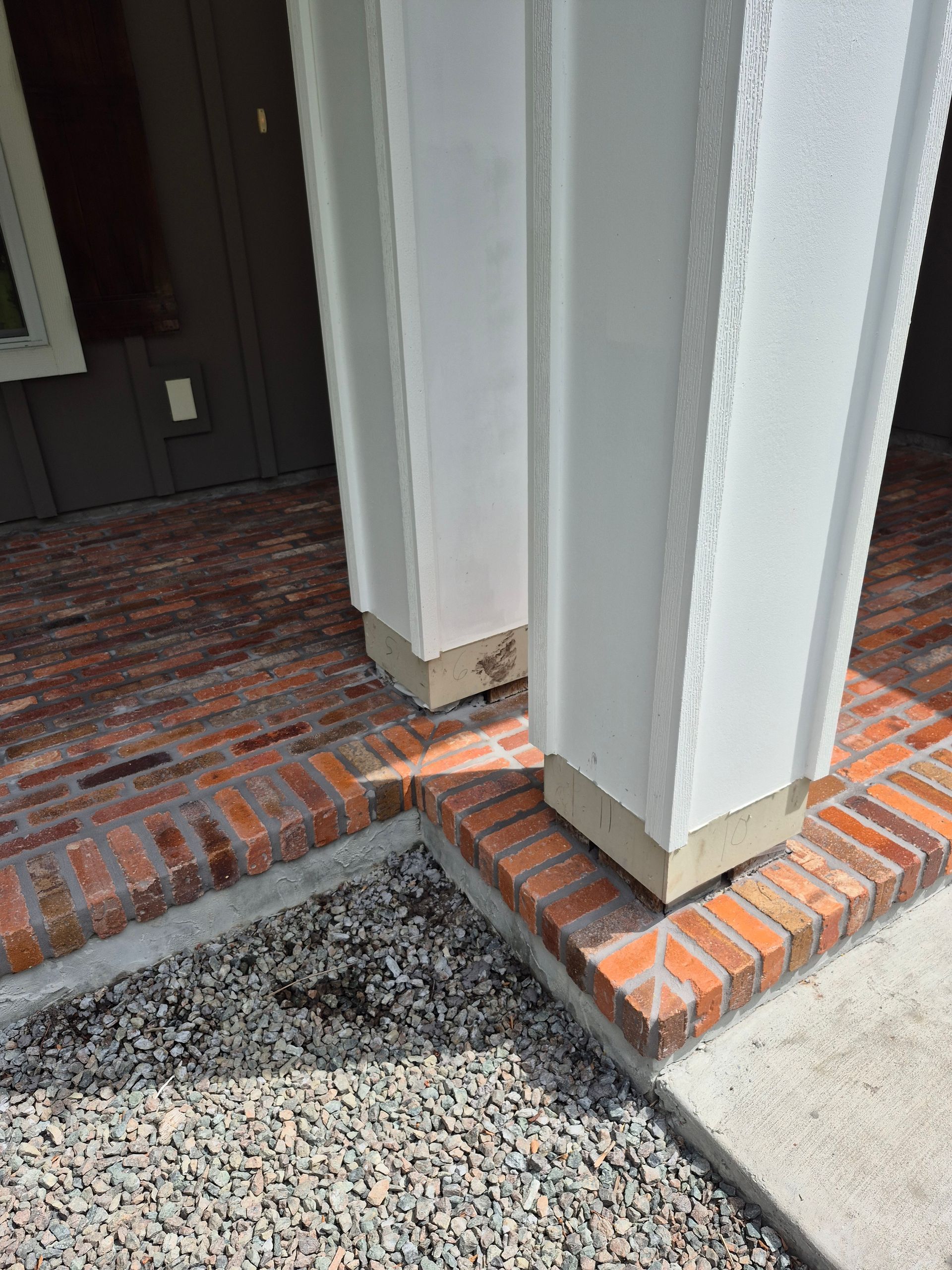 Front porch with white columns on brick bases beside a dark entry door and gravel walkway
