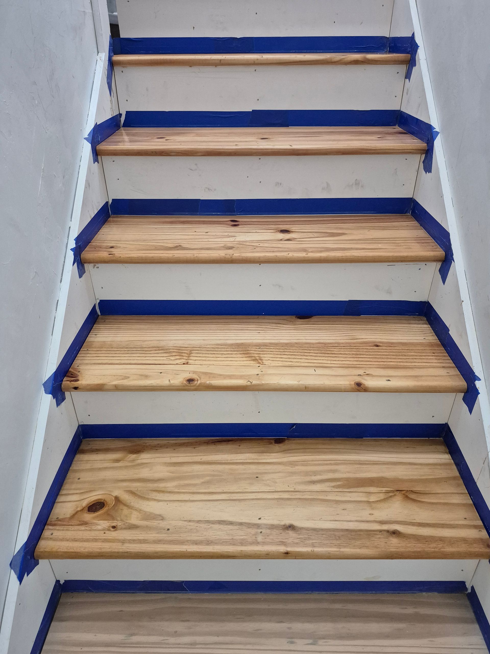 Staircase with unfinished wooden steps and blue-edged tape or trim along the sides, viewed from below