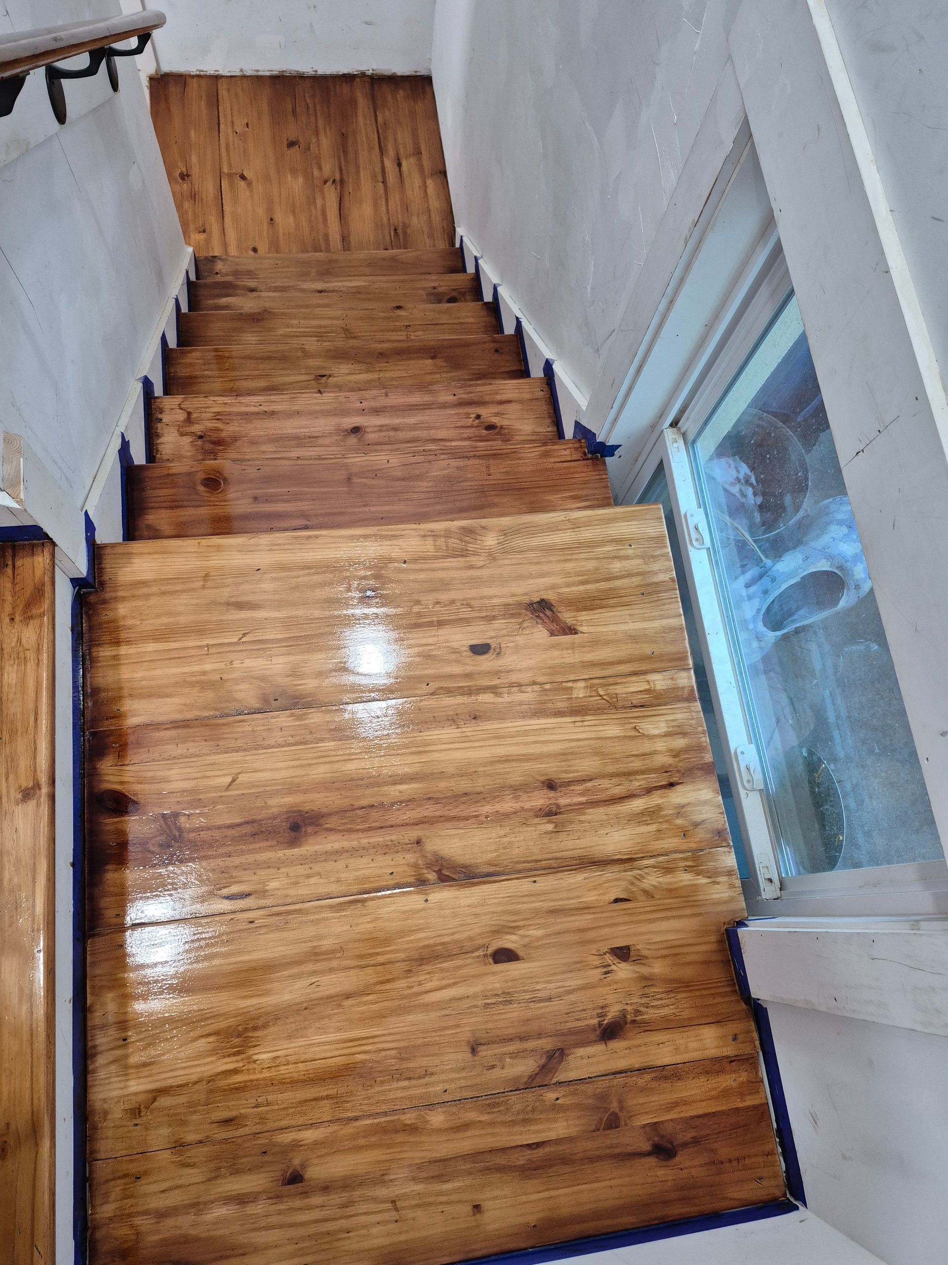 Narrow wooden staircase with white walls and a bright window on the right