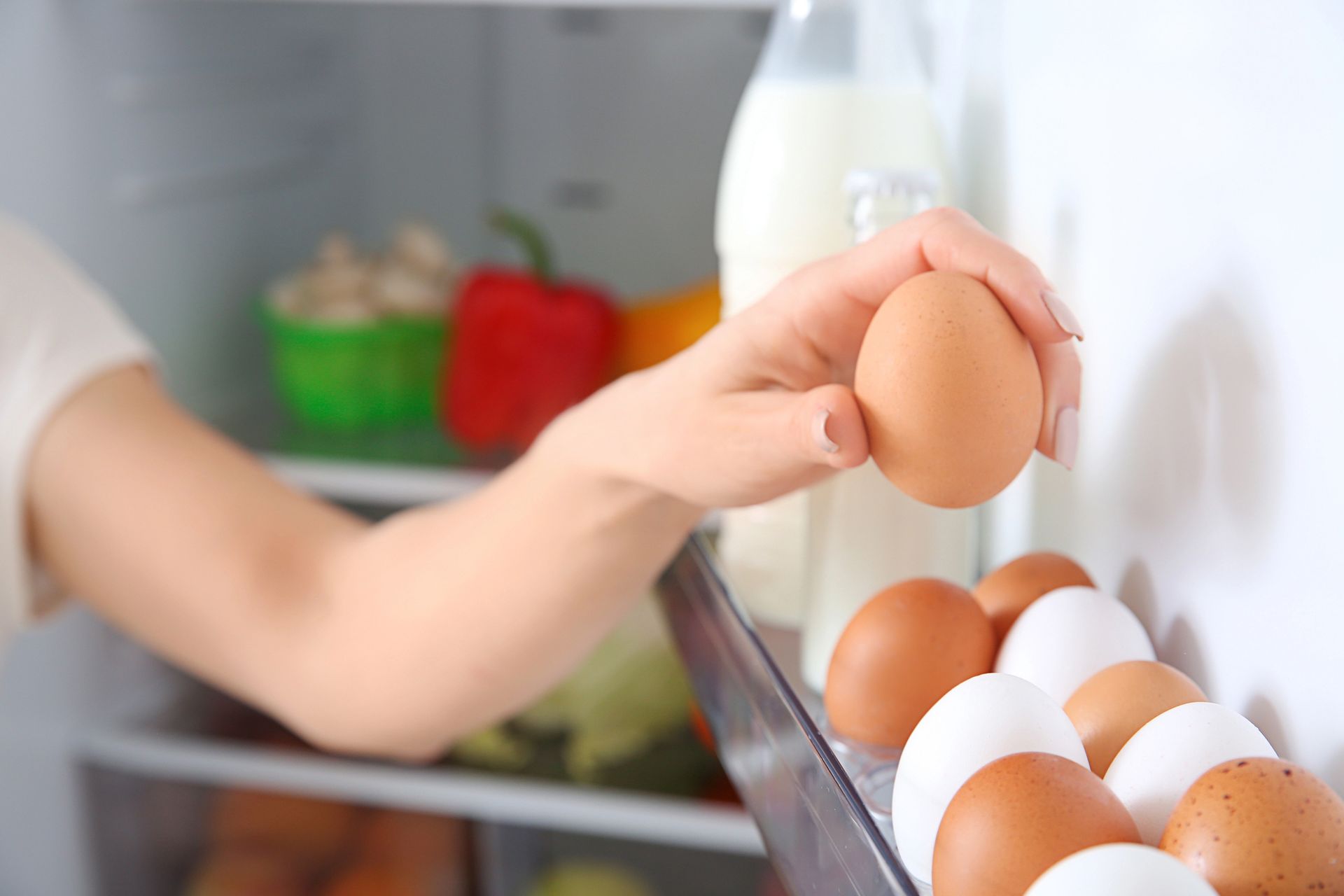 La mano di una persona infila la mano nel frigorifero e prende un uovo da un cartone. Sono visibili altri generi alimentari.