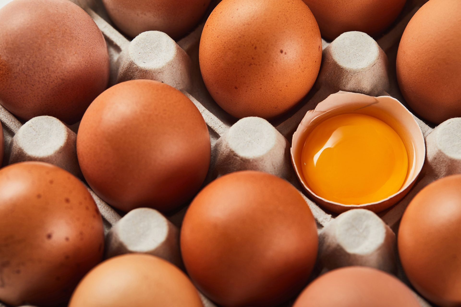 Uova marroni in una scatola di cartone, una delle quali aperta rivela un tuorlo giallo brillante.