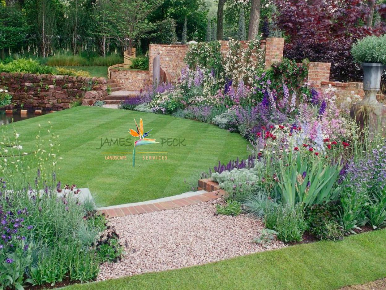 A vibrant garden with a curved lawn, gravel path, and colorful flowerbeds, with a stone wall in the background.