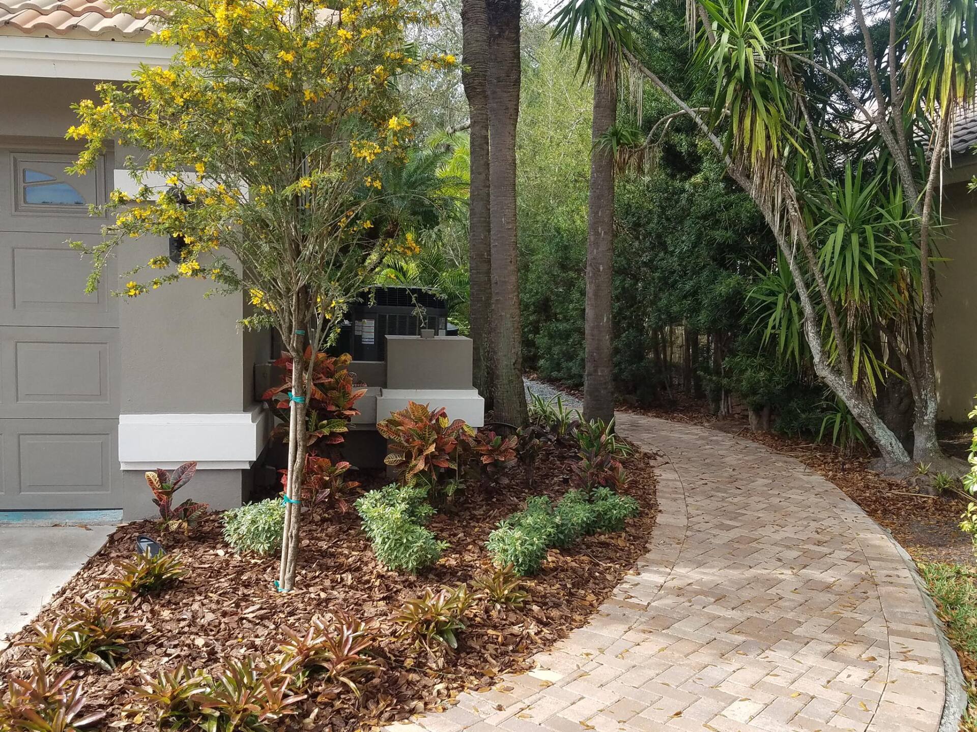 Brick walkway through landscaped yard, leading to a house with a garage.