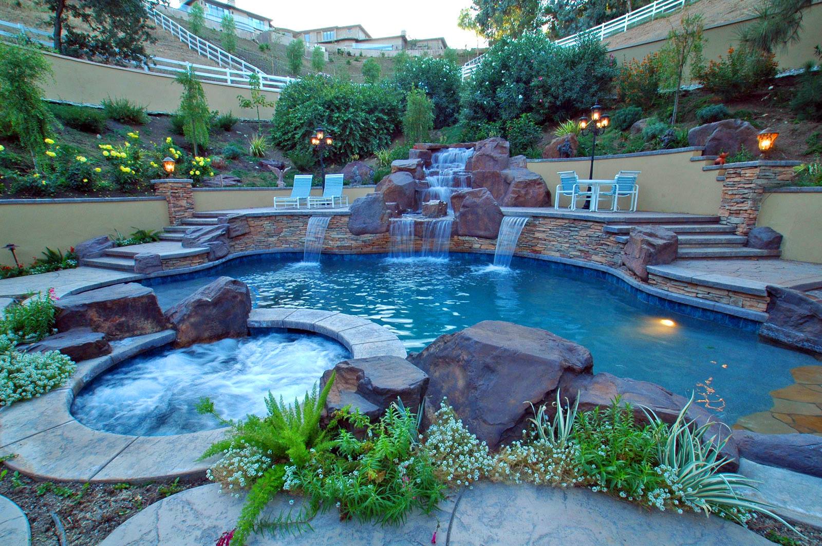 Backyard pool with waterfall and spa, surrounded by landscaping and stone.