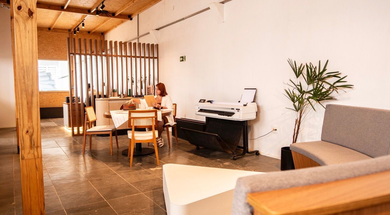 Sala de estar moderna e luminosa com sofá, mesa de jantar, piano e planta de interior sob um teto de madeira.