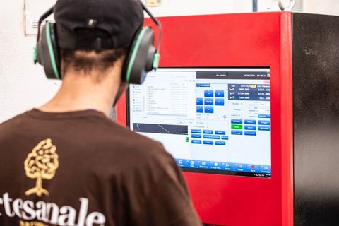 Pessoa usando fones de ouvido em uma estação de trabalho com um computador, com uma divisória vermelha e um software aberto na tela.