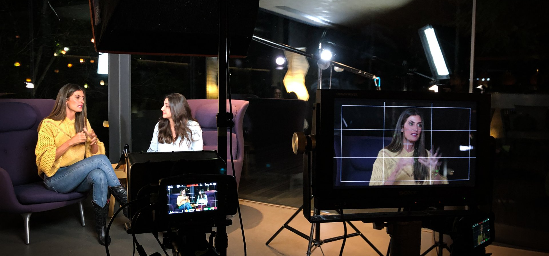 Produção do Curso Online Isabella Fiorentino Duas mulheres estão sentadas em frente a uma câmera conversando.