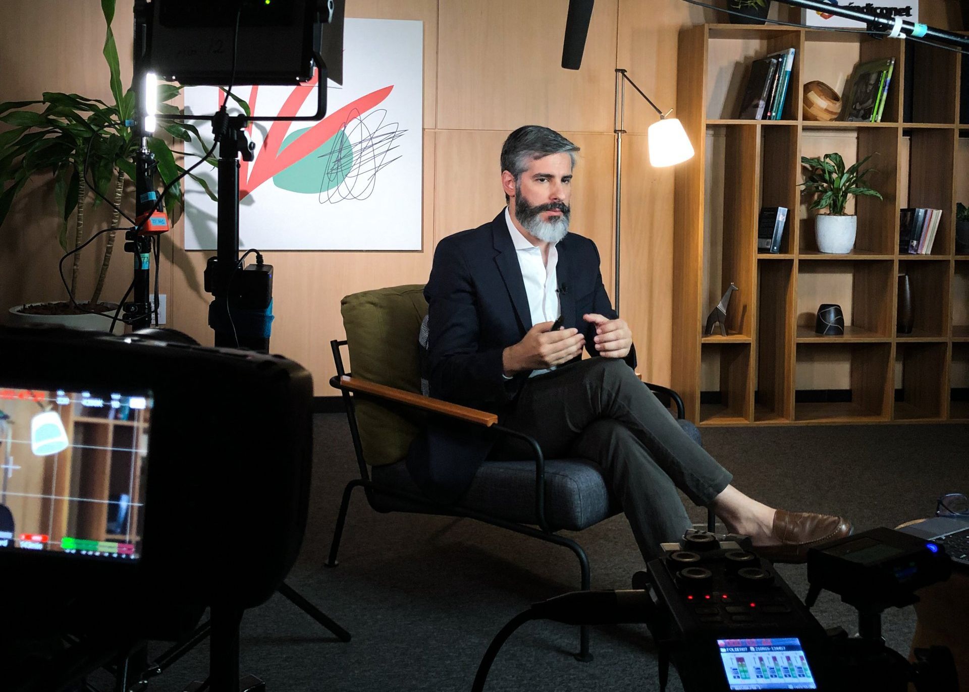 A man with a beard is sitting in a chair in front of a camera.