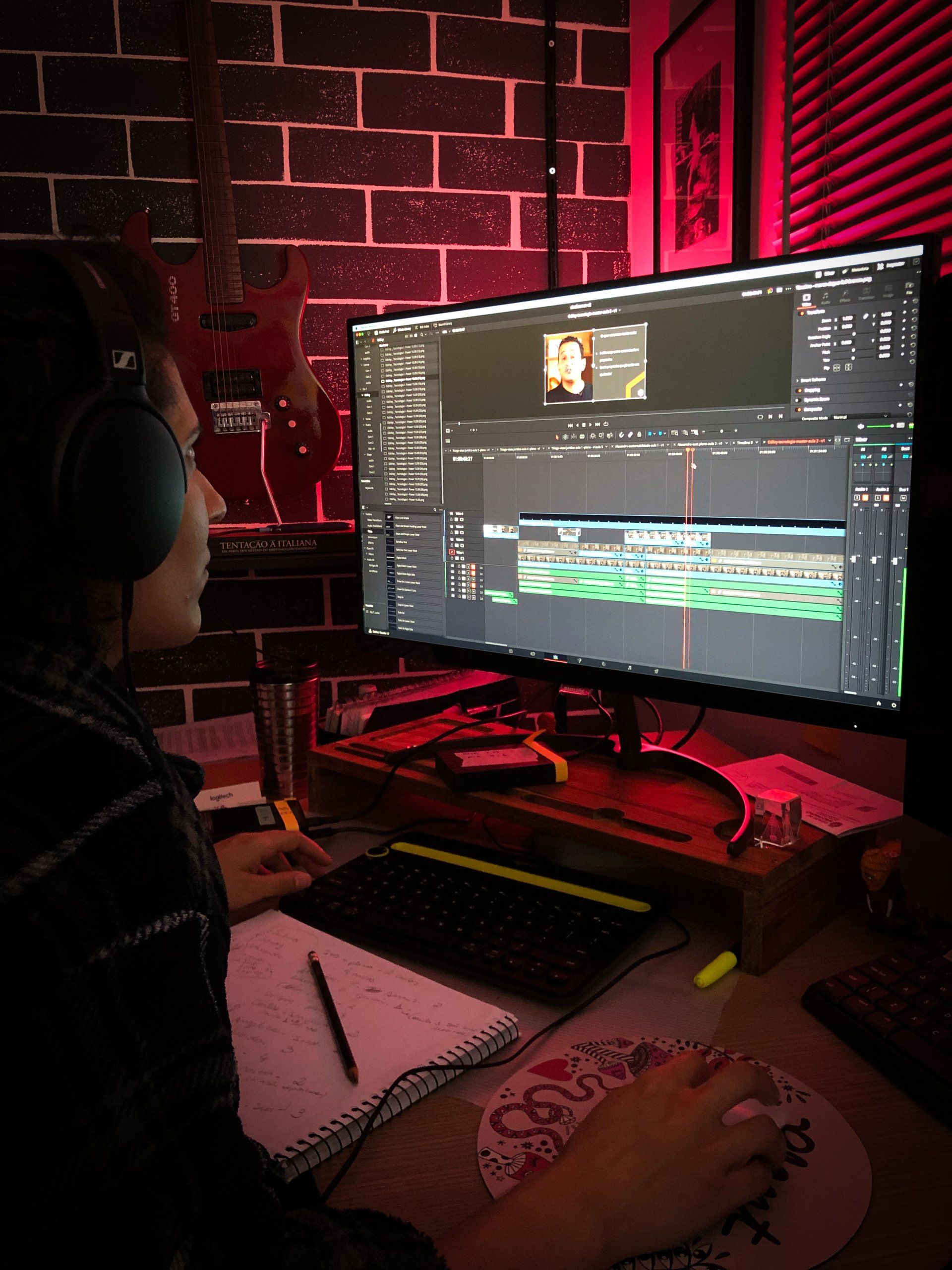 Um homem usando fones de ouvido está sentado em frente a um monitor de computador.