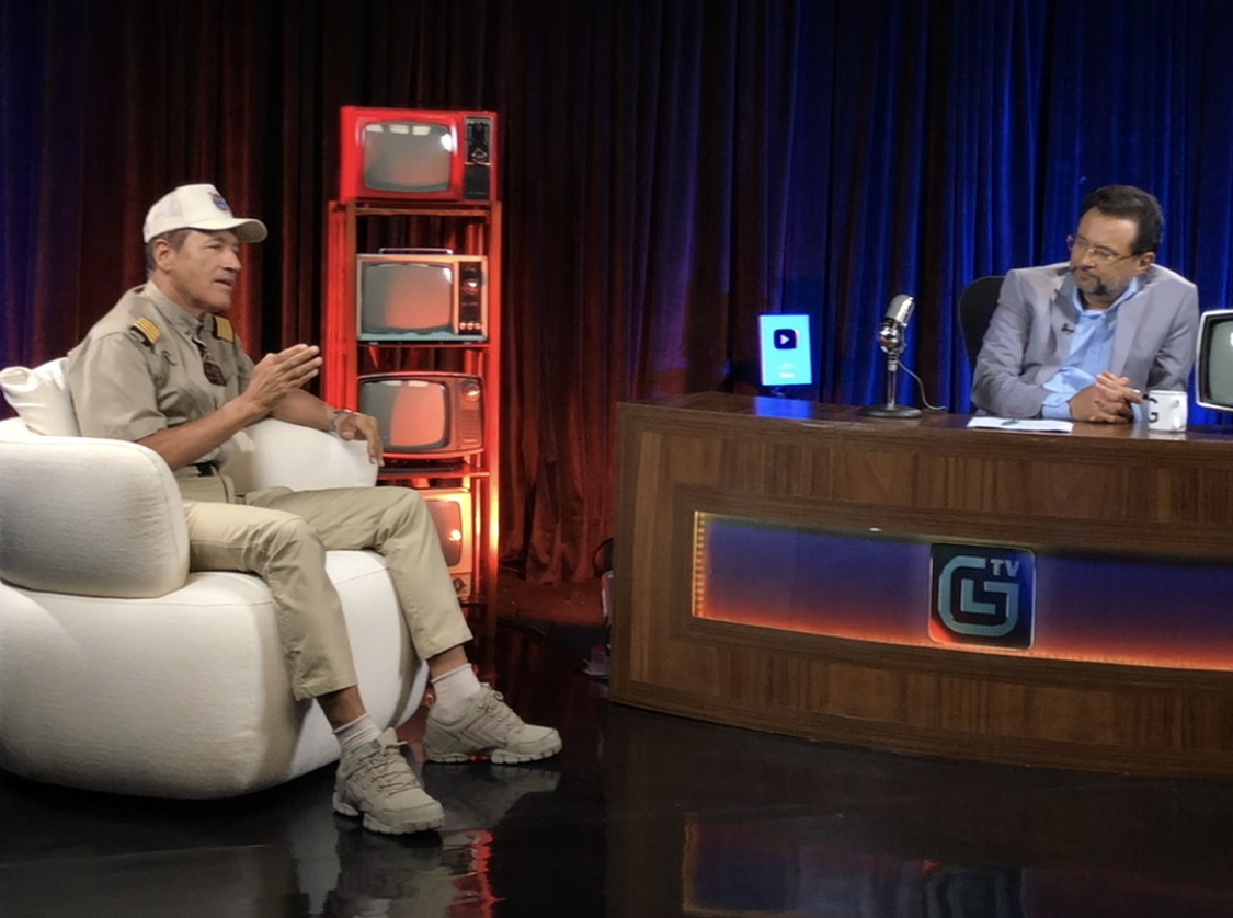 Gravação do TalkShow - Geraldo Luis TV | TAG12 Talk show interview: guest in white cap speaks on couch while host sits at desk on stage.