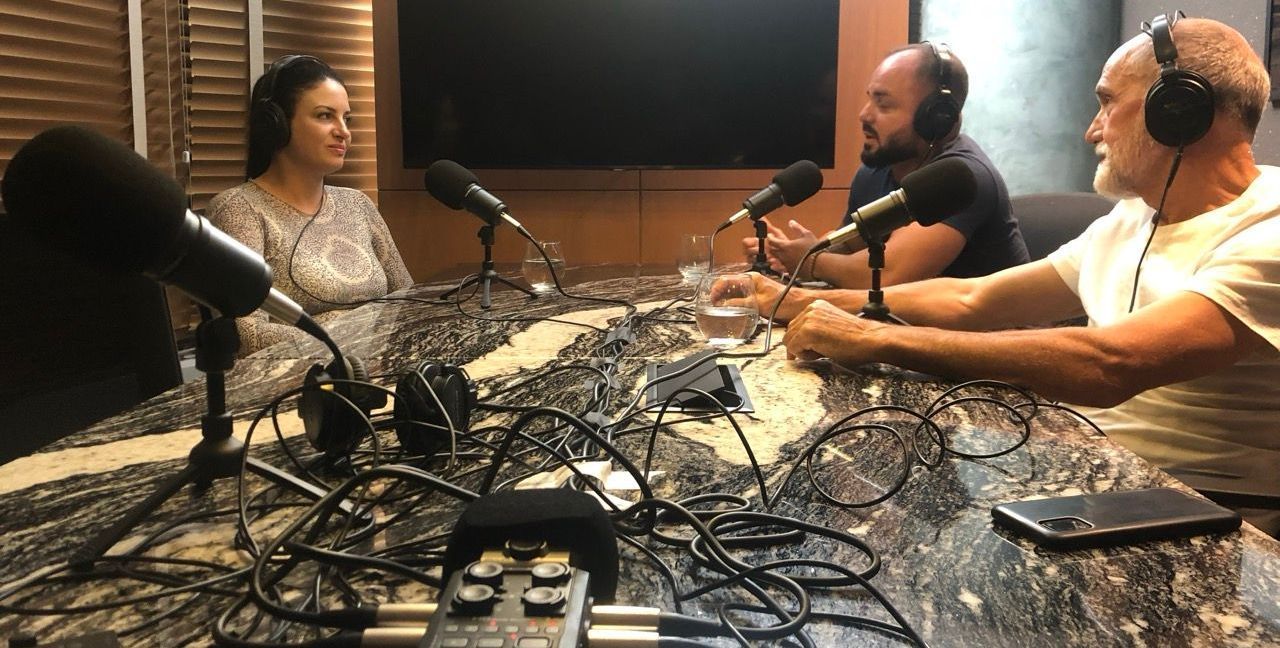 Gravamos e editamos o podcast da sua empresa Um grupo de pessoas está sentado em uma mesa em frente a microfones.