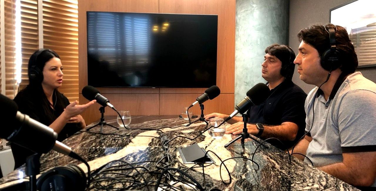 Gravamos e editamos o Podcast da sua empresa Um grupo de pessoas está sentado em uma mesa em frente a microfones.