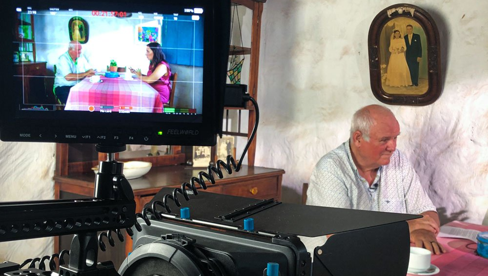 Gravação do curso - Além da biografia - Da Capo Um homem está sentado à mesa em frente à televisão.