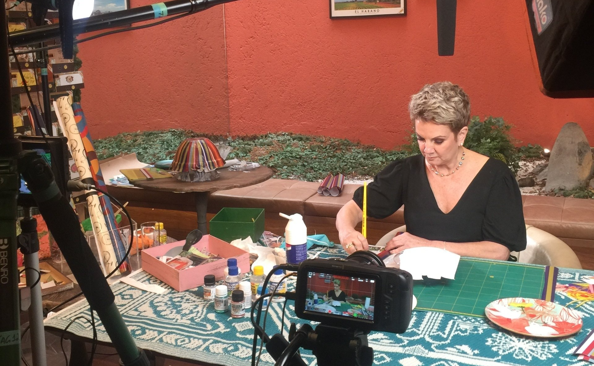 Uma mulher está sentada em uma mesa pintando com uma câmera atrás dela.