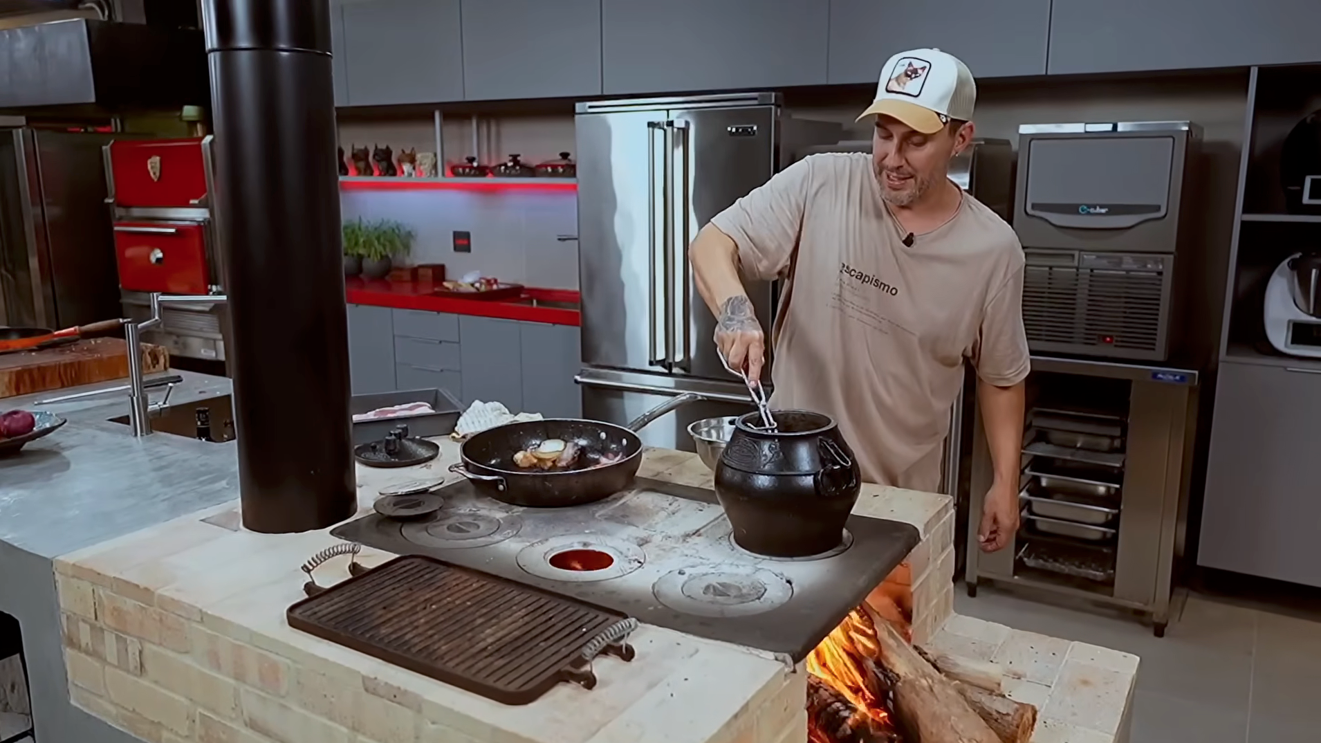 Chef stirring pots over an outdoor wood-fired stove in a kitchen, with flames visible underneath.