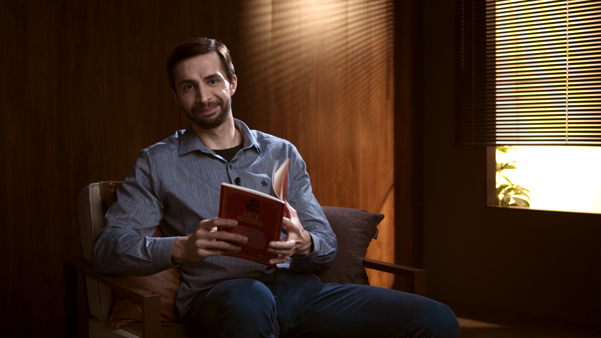 Um homem está sentado em uma cadeira segurando um livro.