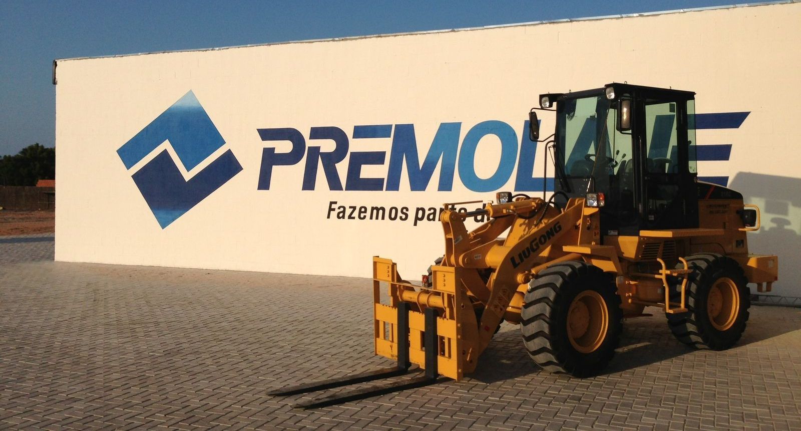 Produção do vídeo institucional da Premolaje A yellow forklift is parked in front of a white wall that says premolate