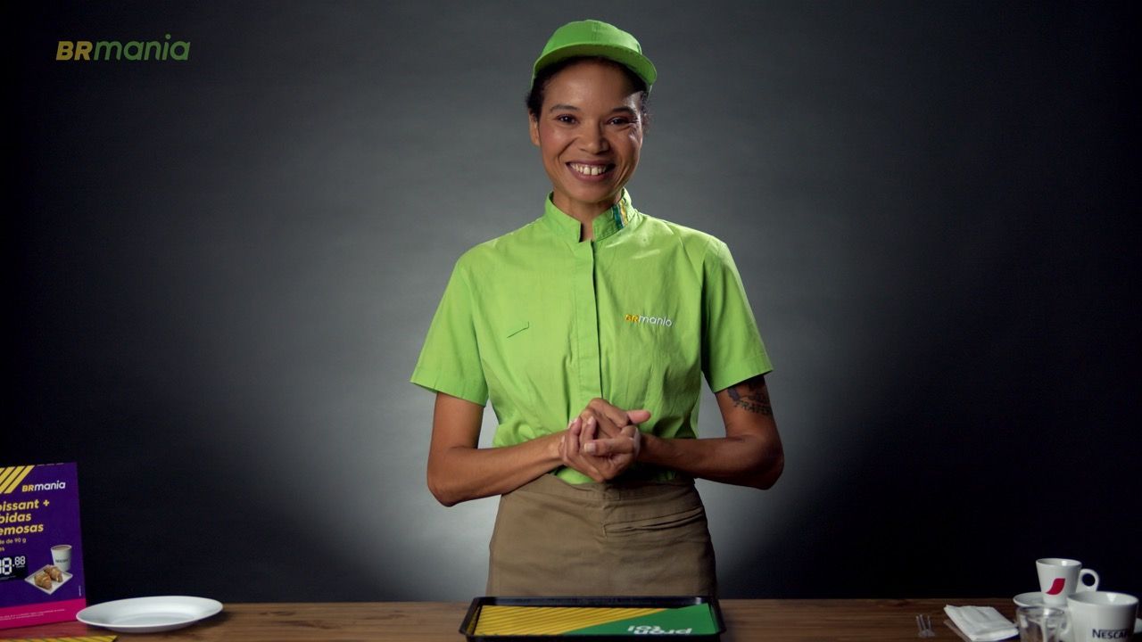 Uma mulher de camisa verde e chapéu está parada em frente a uma mesa.