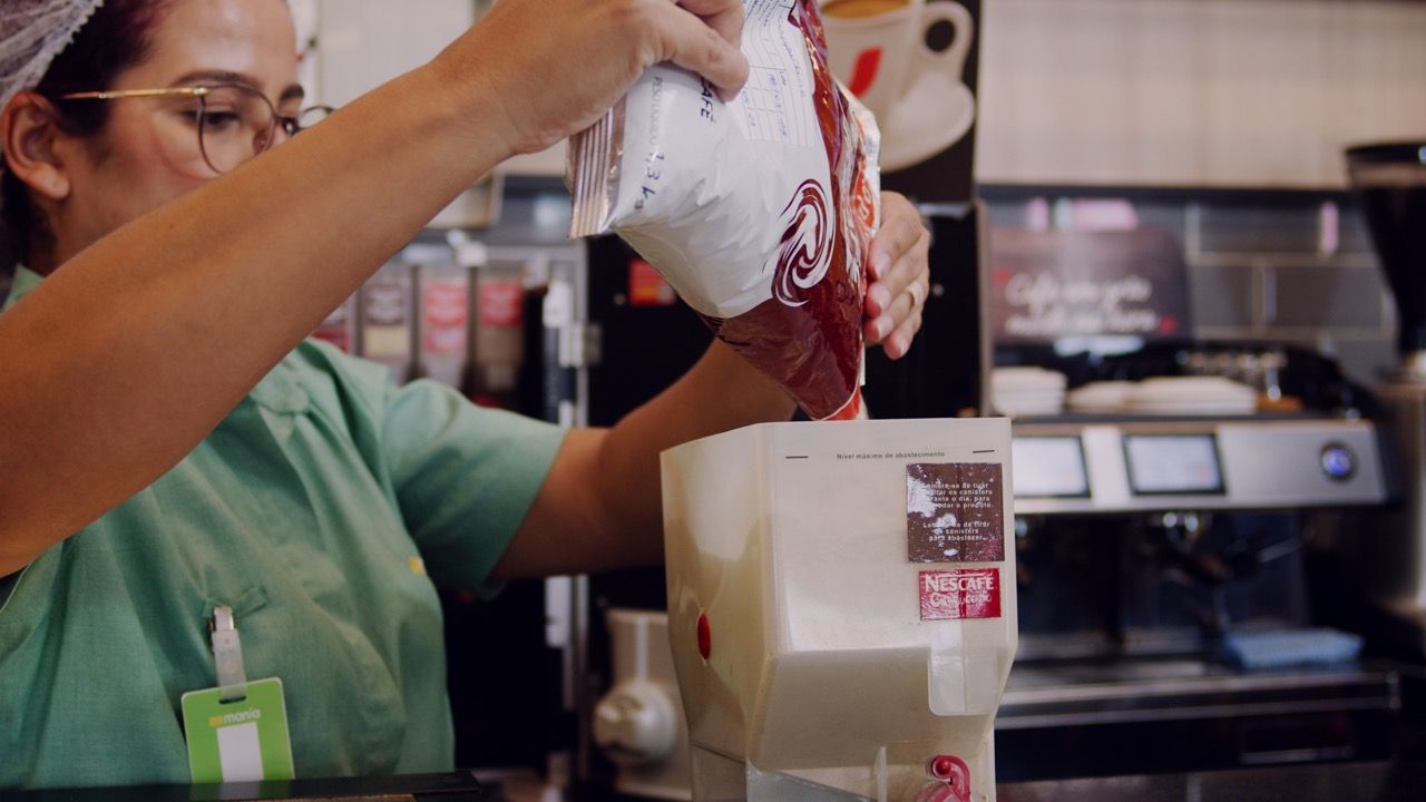 Treinamento EaD - BRMania Uma mulher está colocando leite no liquidificador em um restaurante.