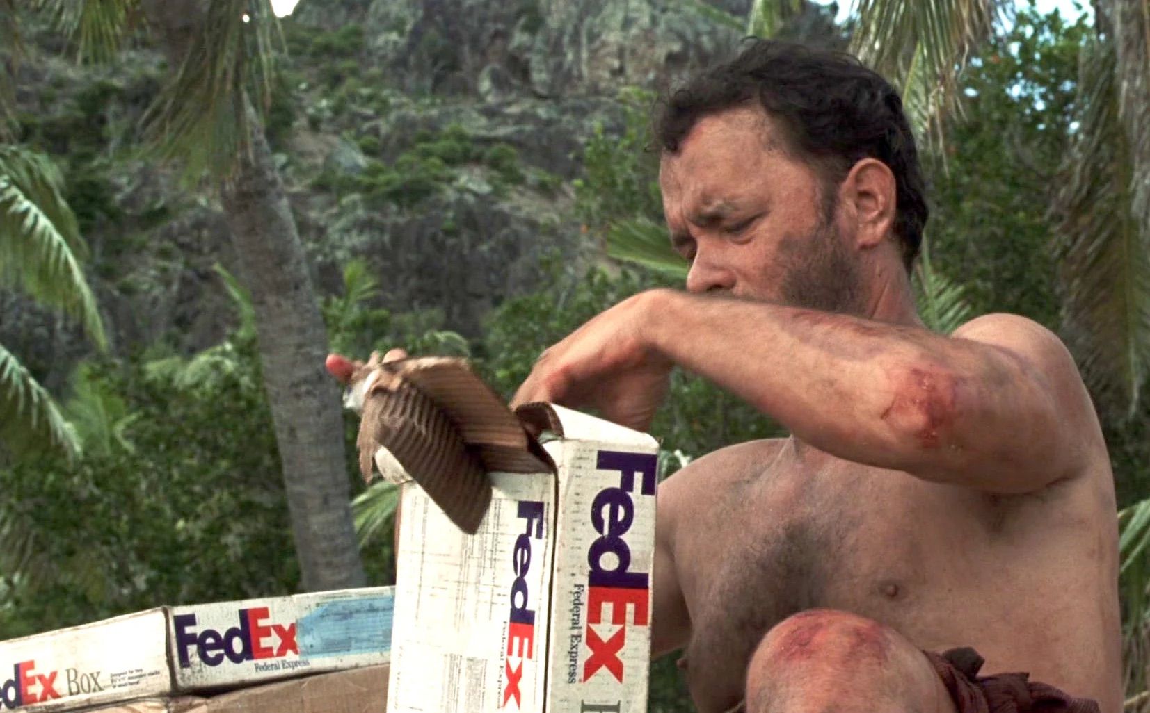 Um homem sem camisa está abrindo uma caixa Fedex na selva.