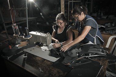 Duas mulheres trabalham em uma máquina de costura em um quarto escuro.