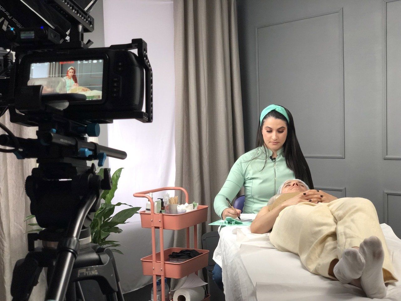 Uma mulher está fazendo um tratamento facial em um homem na frente de uma câmera.