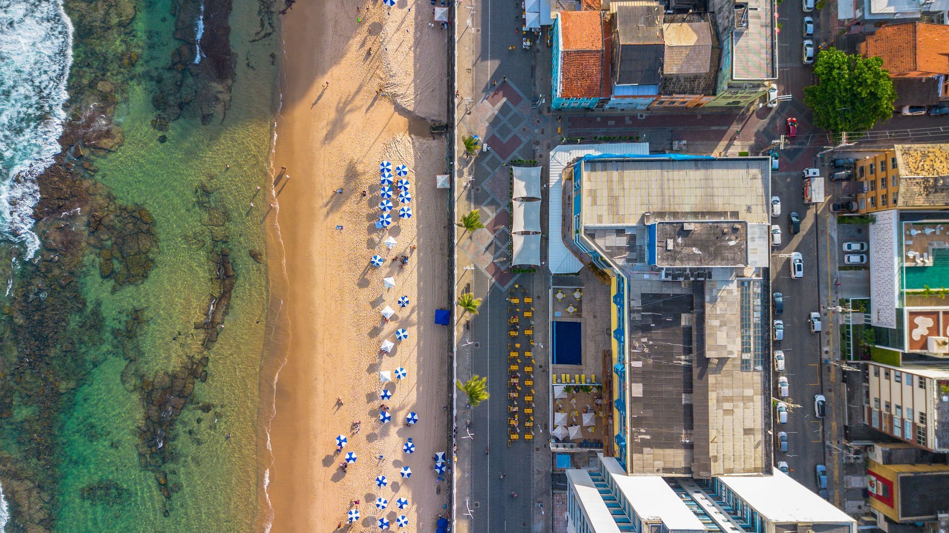 Aerial view of a crowded beach beside buildings and green-blue ocean water