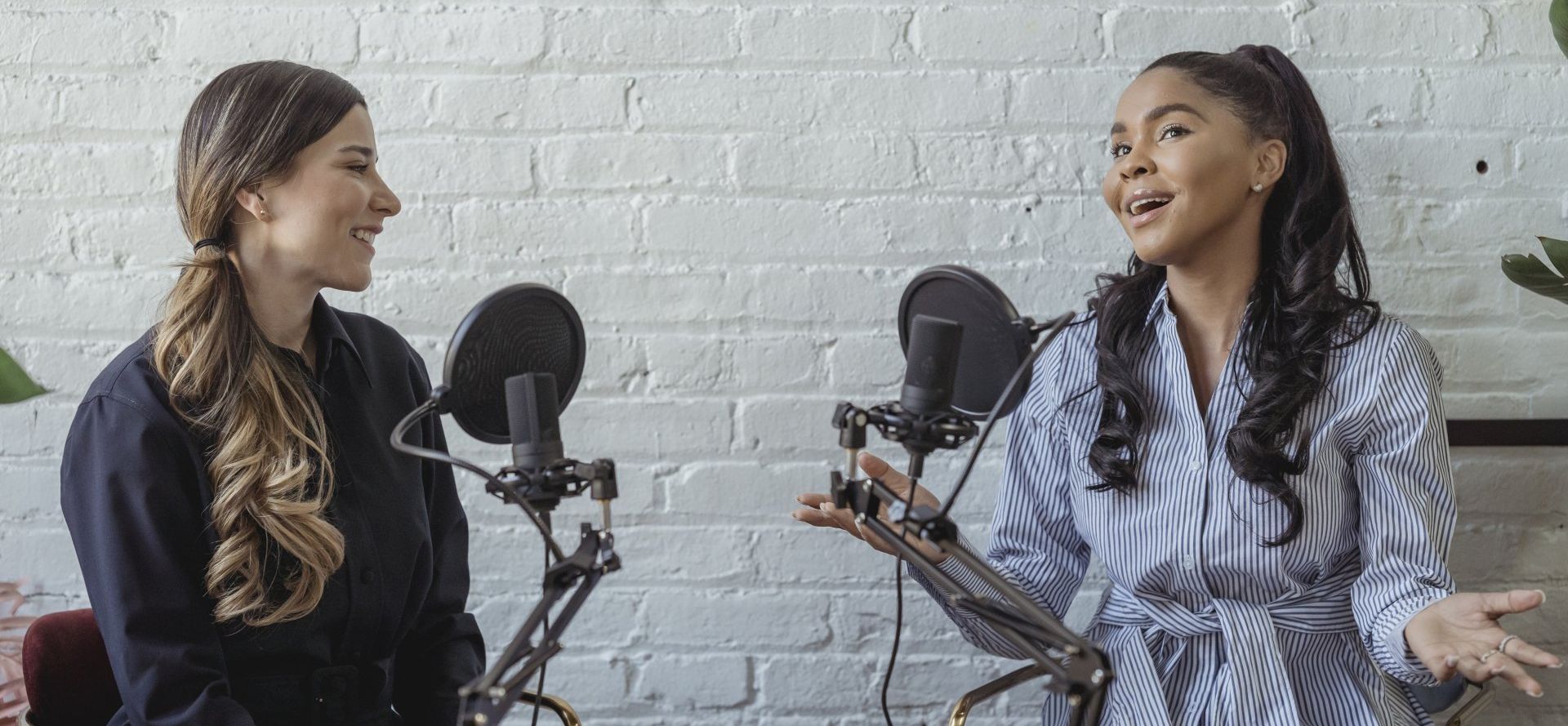 Two women are sitting in front of microphones talking to each other.