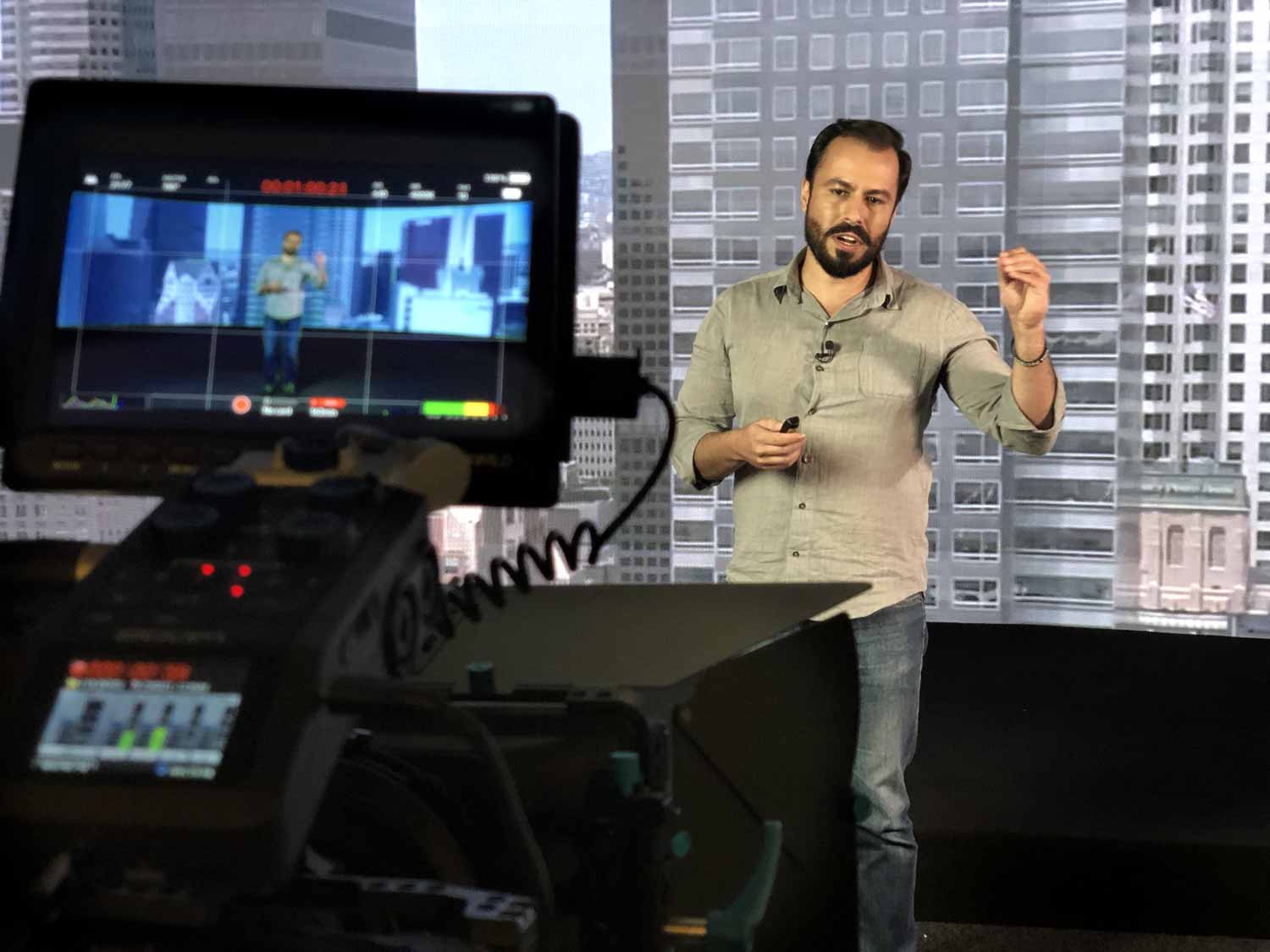 Treinamento Corporativo EaD Um homem está parado na frente de uma câmera com uma cidade ao fundo