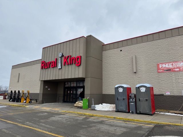 Rural King store exterior with porta-potties. Red sign, overcast sky, snow patches on ground.