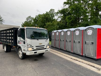 A dump truck is parked next to a row of portable toilets.