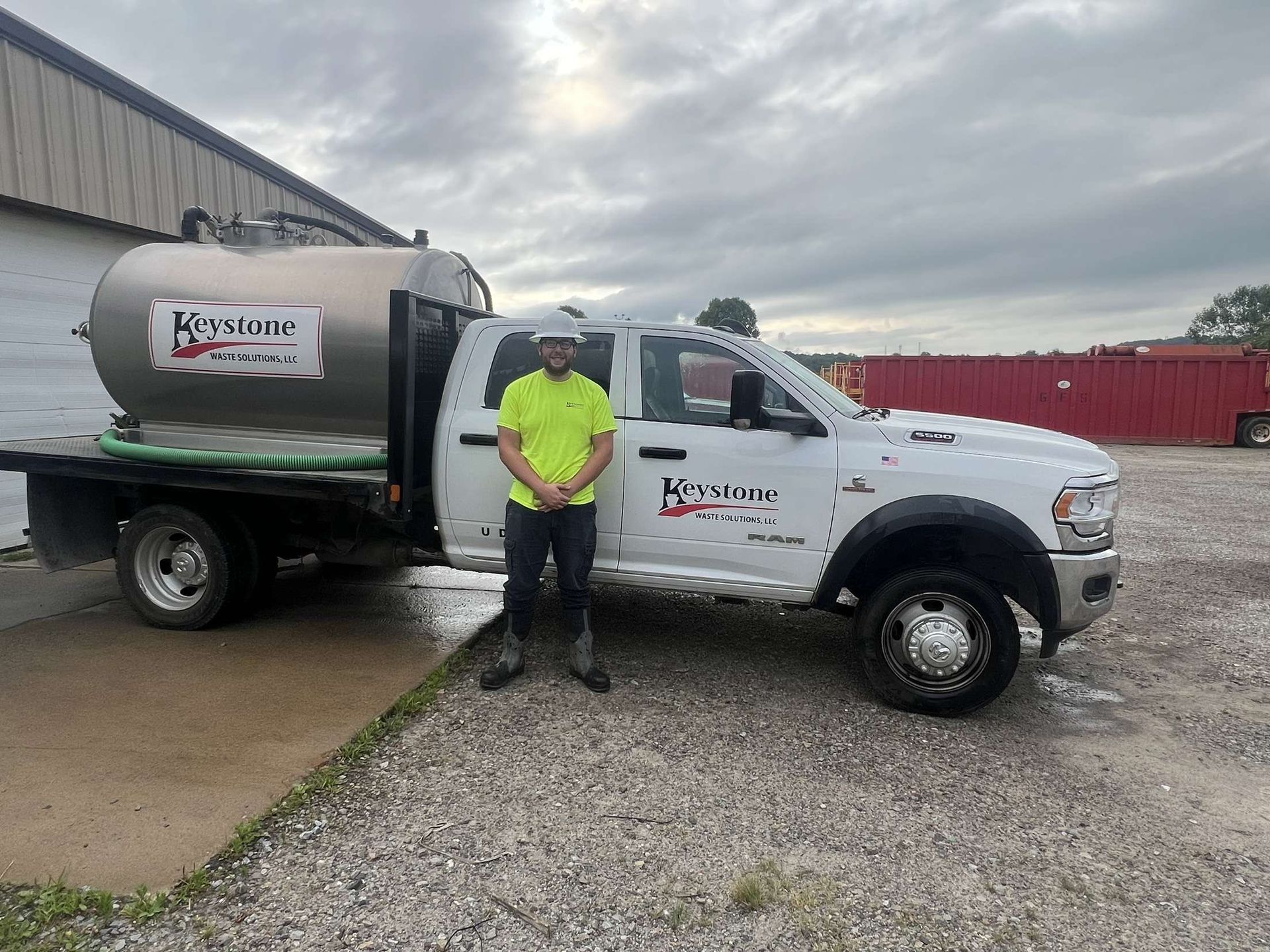 Man in front of white truck with water tank. Gray tank has logo. Cloudy sky, gravel ground. | Keystone Waste Solutions