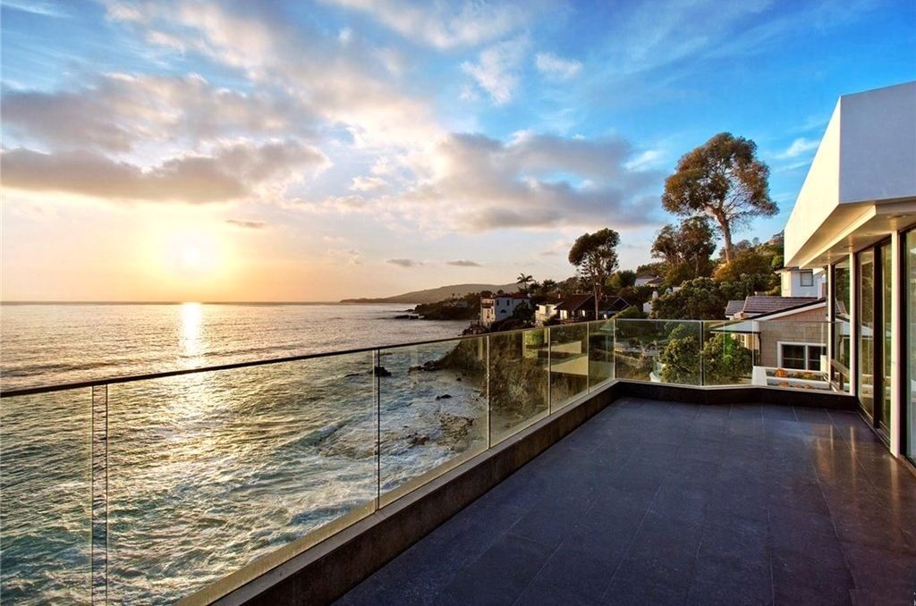Ocean view from a modern house terrace at sunset. The sky is golden and blue with calm water.