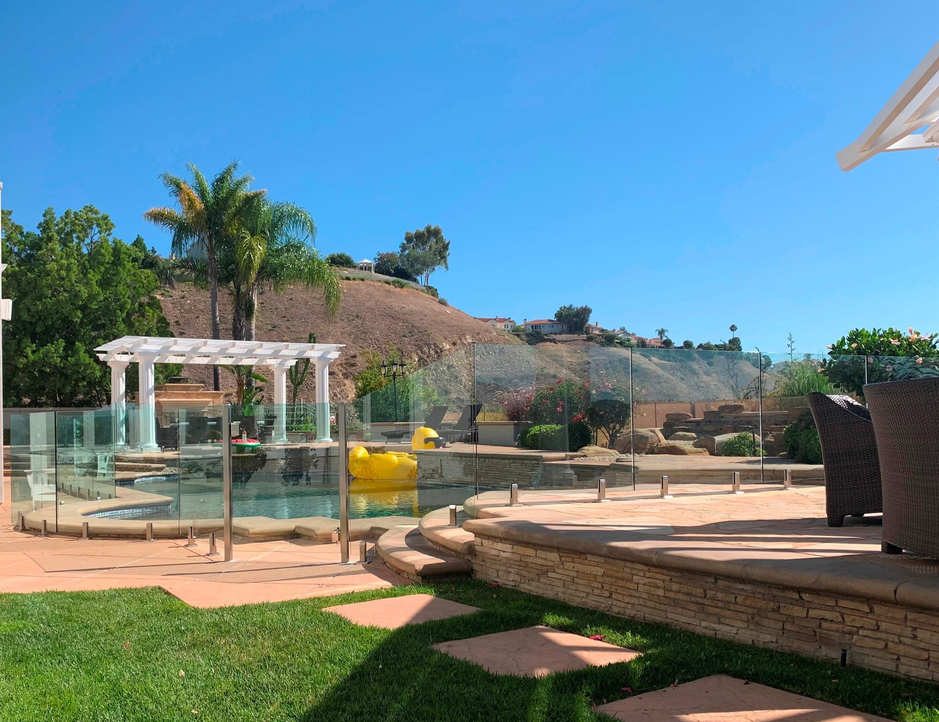 Backyard with pool, pergola, steps, and distant hillside under blue sky.