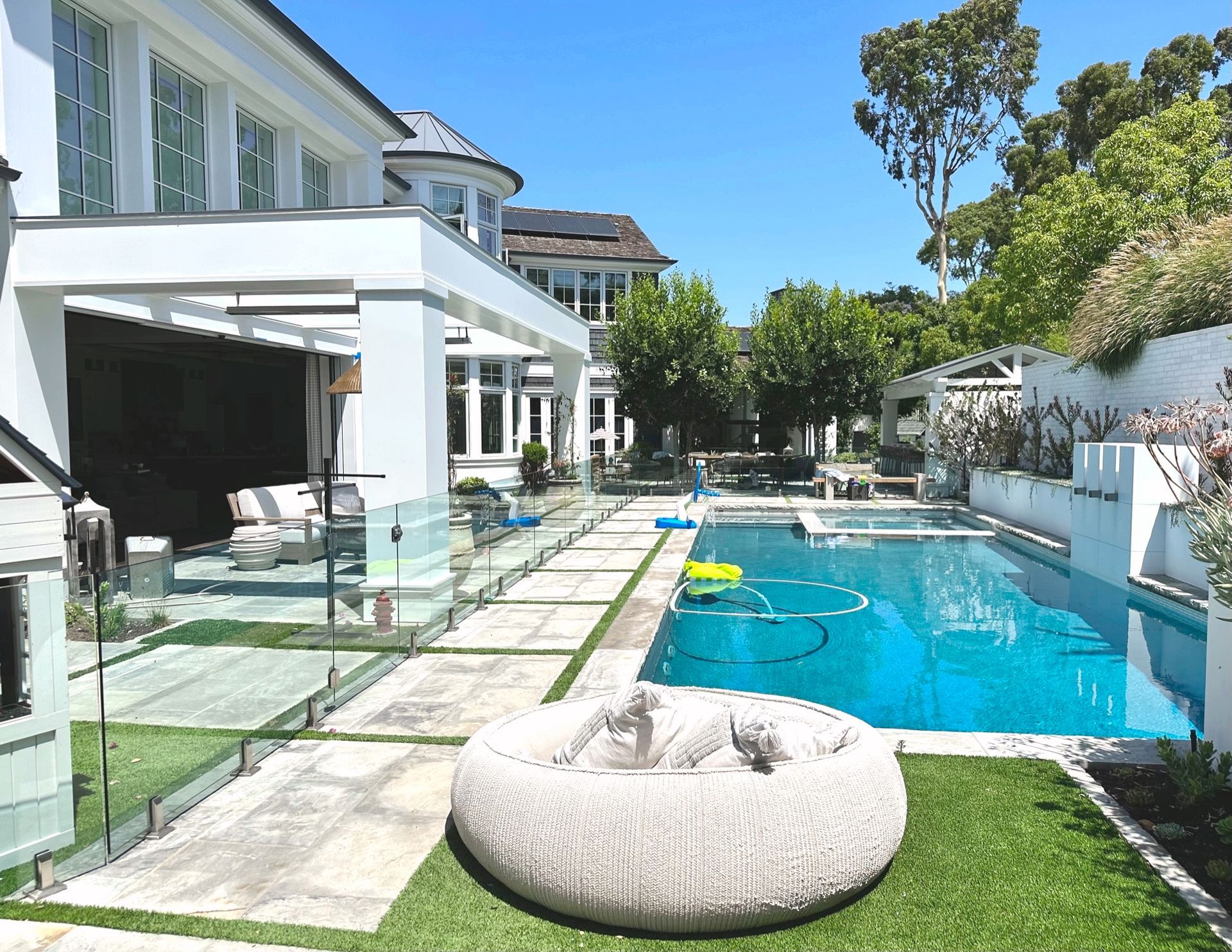 Large white house with pool, patio, and lush green lawn on a sunny day.