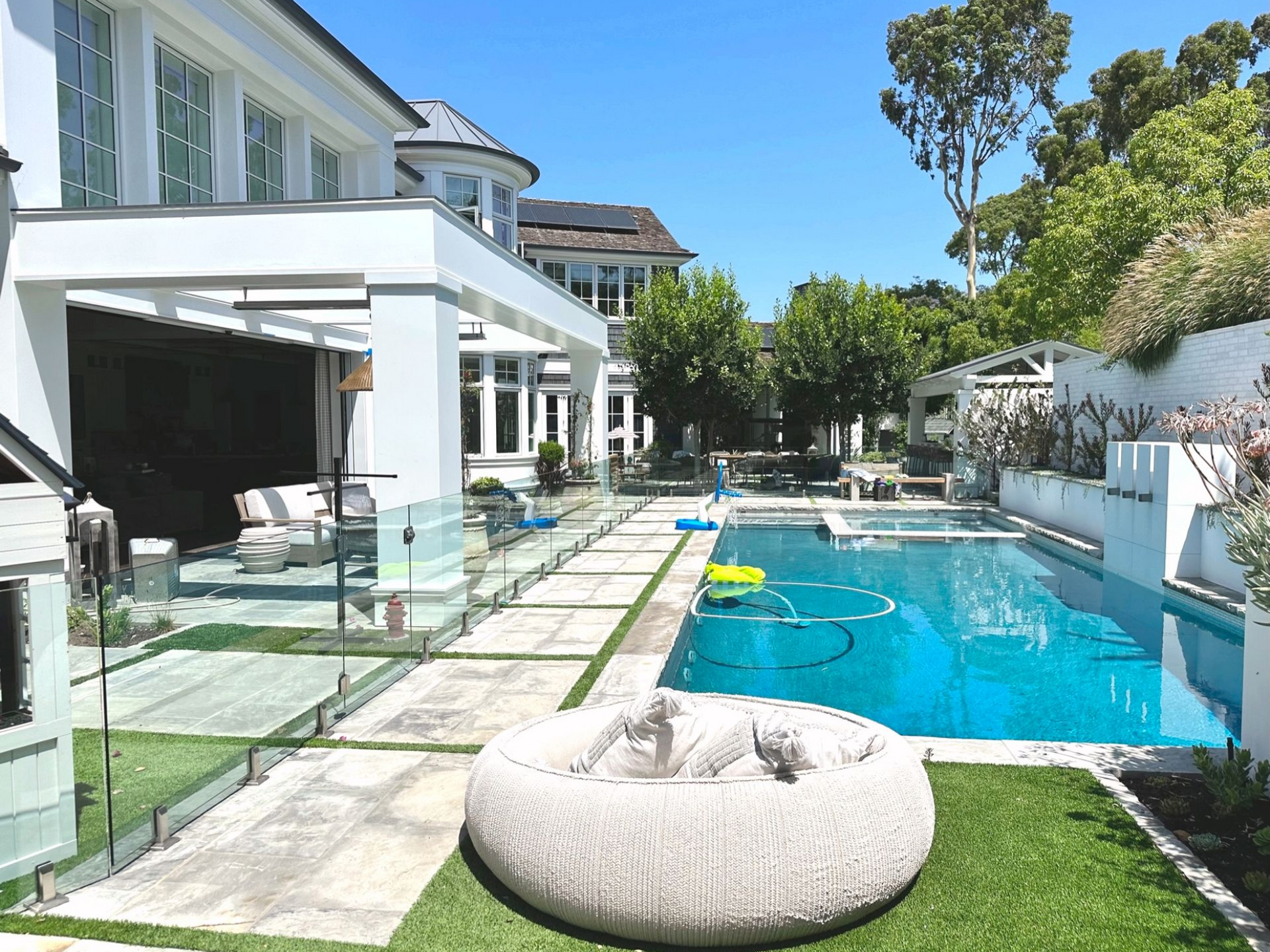 Luxury home exterior with a pool, patio furniture, and lush landscaping on a sunny day.